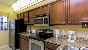 A compact kitchen with wooden cabinets, a refrigerator, a microwave, a stove, a coffee maker, and a window with a view of the outside. - Spacious 3-bedroom condo with AC in beautiful Orlando (Orlando)