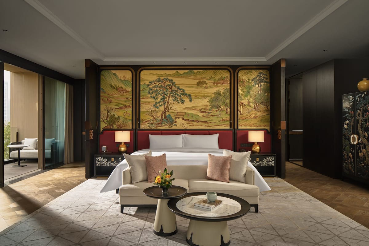Une chambre d’hôtel avec un grand lit, deux tables de chevet, un canapé, une table basse et un grand tableau décoratif au mur.