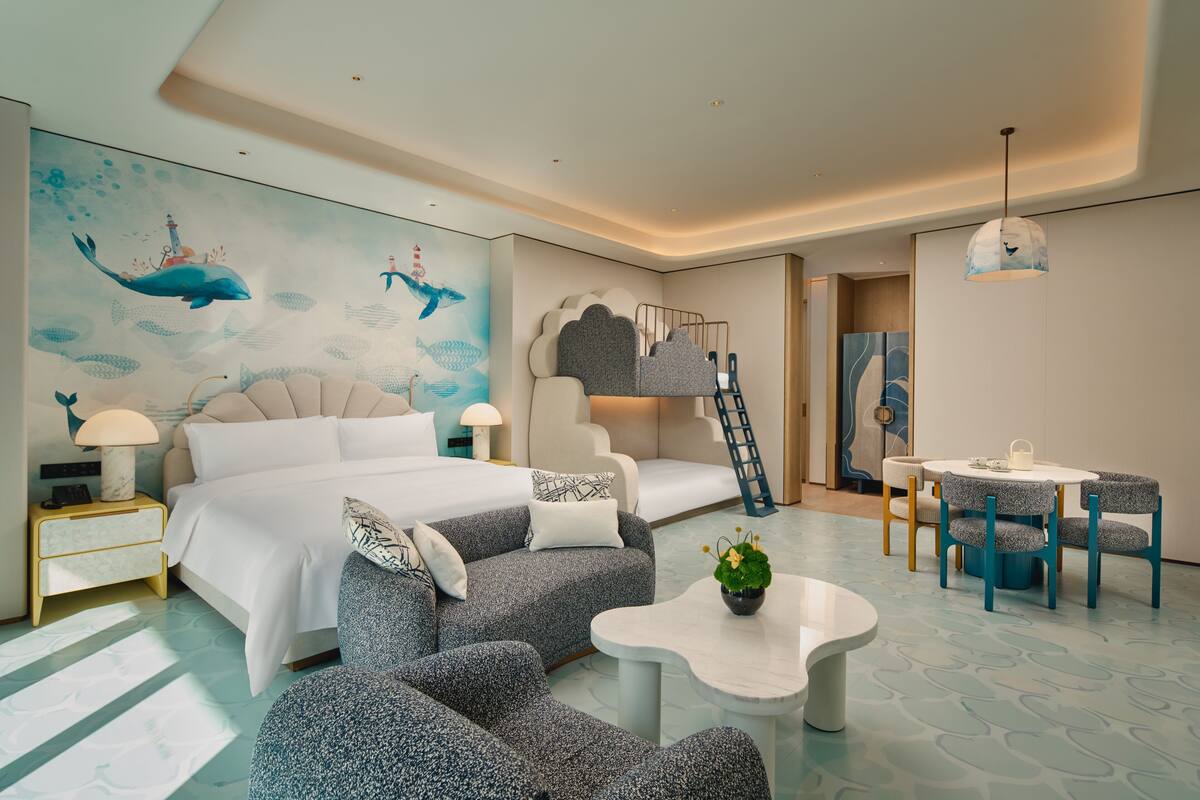 Une chambre d’hôtel moderne comprenant un lit, un canapé, des fauteuils, une petite table et une fresque représentant des créatures marines.