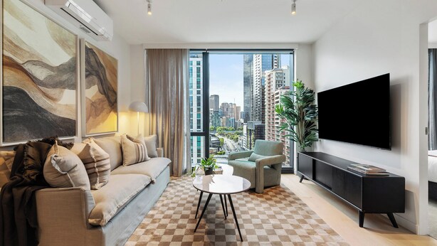 A modern living room with a sofa, a coffee table, a TV, and a view of the cityscape. - Iconic Queensbridge New Designer Suite with Heated Pool, Gym, Sauna, and Steam (Melbourne)