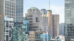 A cityscape with modern buildings, a tram, and a view from a window with a chair. - Iconic Queensbridge New Designer Suite with Heated Pool, Gym, Sauna, and Steam (Melbourne)