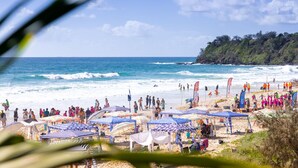 Una playa con sombrillas y gente, cielo despejado y olas.