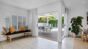 Una sala moderna con sofá, mesa de comedor y un amplio ventanal corredera que da a un área exterior con piscina.