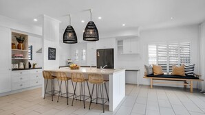 Una cocina moderna con una isla central, armarios blancos y una zona de estar con un banco y cojines.