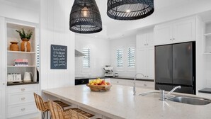 Una cocina moderna con armarios blancos, una isla grande con taburetes y un refrigerador negro, además de un lámpara colgante.