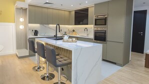 Une cuisine moderne dotée d’un îlot en marbre, de deux tabourets de bar, d’appareils électroménagers intégrés et d’un mur d’accent jaune.