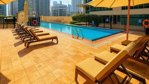 Une piscine sur le toit, dotée de chaises longues et de parasols, entourée d’immeubles de grande hauteur.