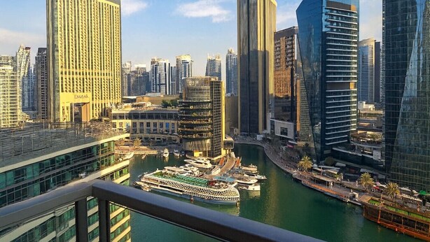 Un paysage urbain avec des immeubles modernes de grande hauteur, une marina avec des bateaux et une vue dégagée sur l’eau.