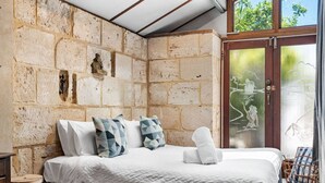 Ein Schlafzimmer mit Steinwand, einem Bett mit weißer Bettwäsche und Blick auf ein Wasserelement durch eine Glastür.