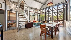 Ein geräumiges Zimmer mit einer Wendeltreppe, großen Fenstern und einer Essecke mit Stühlen und Tisch.