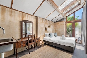 A bedroom with a bed, a desk with a mirror, a chair, a sink, and a large window.