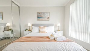 Quarto de hotel com uma cama grande, duas mesas de cabeceira com luminárias, um espelho e um quadro na parede.