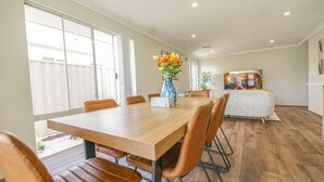 A dining area with a wooden table, brown leather chairs, a vase with flowers, and a TV in the background. - StayAU 5 Beds Pet-friendly Haven Escape in WA (Secret Harbour)
