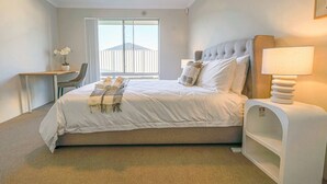 A hotel room with a bed, a desk, a chair, a lamp, and a window with a view of a building. - StayAU 5 Beds Pet-friendly Haven Escape in WA (Secret Harbour)