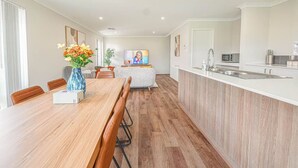 A modern kitchen with a central island, a dining area with a wooden table, and a living area with a sofa and TV. - StayAU 5 Beds Pet-friendly Haven Escape in WA (Secret Harbour)