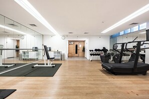 Ein Fitnessraum mit Trainingsgeräten, einer Spiegelwand und Holzboden.