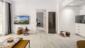 Une cuisine moderne avec des meubles blancs, un réfrigérateur en acier inoxydable et un coin repas comprenant une table en bois et un tableau représentant un paysage.