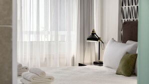 Un lit bien fait, avec du linge de lit blanc, une lampe de bureau noire et un coussin vert.