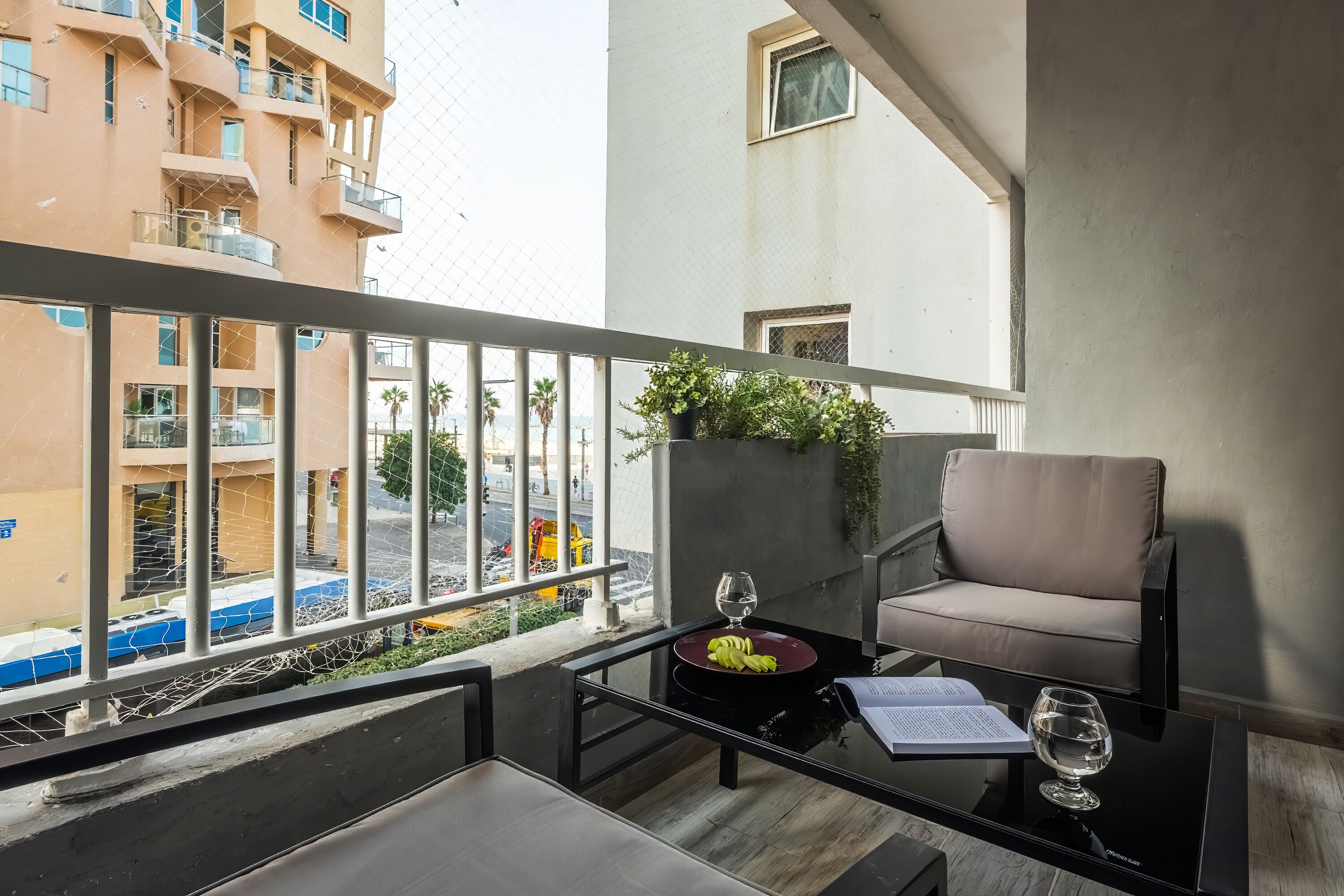 Un balcone con un tavolo in vetro, una divano e una pianta in vaso.