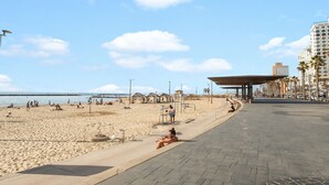 Une plage avec une promenade dallée, des parasols et des palmiers.