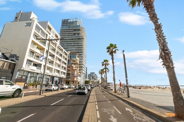 Eine Straße mit Radweg, Palmen und einem Strand im Hintergrund.