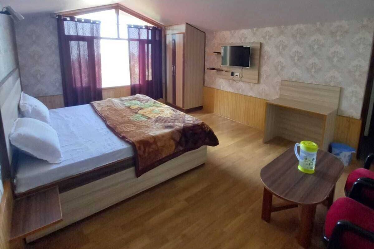 A bedroom with a bed, a TV, a small table, and a chair.