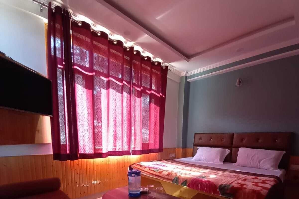 A hotel room with a bed, a sofa, a small table with a water bottle, and a TV mounted on the wall.