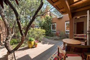 A patio area with a wooden table and chairs, surrounded by potted plants and a view of a building. - Cinco Chimineas- Indoor Pool, Walk to Plaza (Santa Fe)