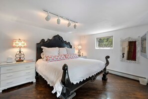 A bedroom with a large bed, two bedside tables, a nightstand, a decorative mirror, and a window with a view. - Cinco Chimineas- Indoor Pool, Walk to Plaza (Santa Fe)