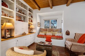 A cozy living room with a sofa, a chair, a coffee table, and a bookshelf filled with decorative items. - Cinco Chimineas- Indoor Pool, Walk to Plaza (Santa Fe)