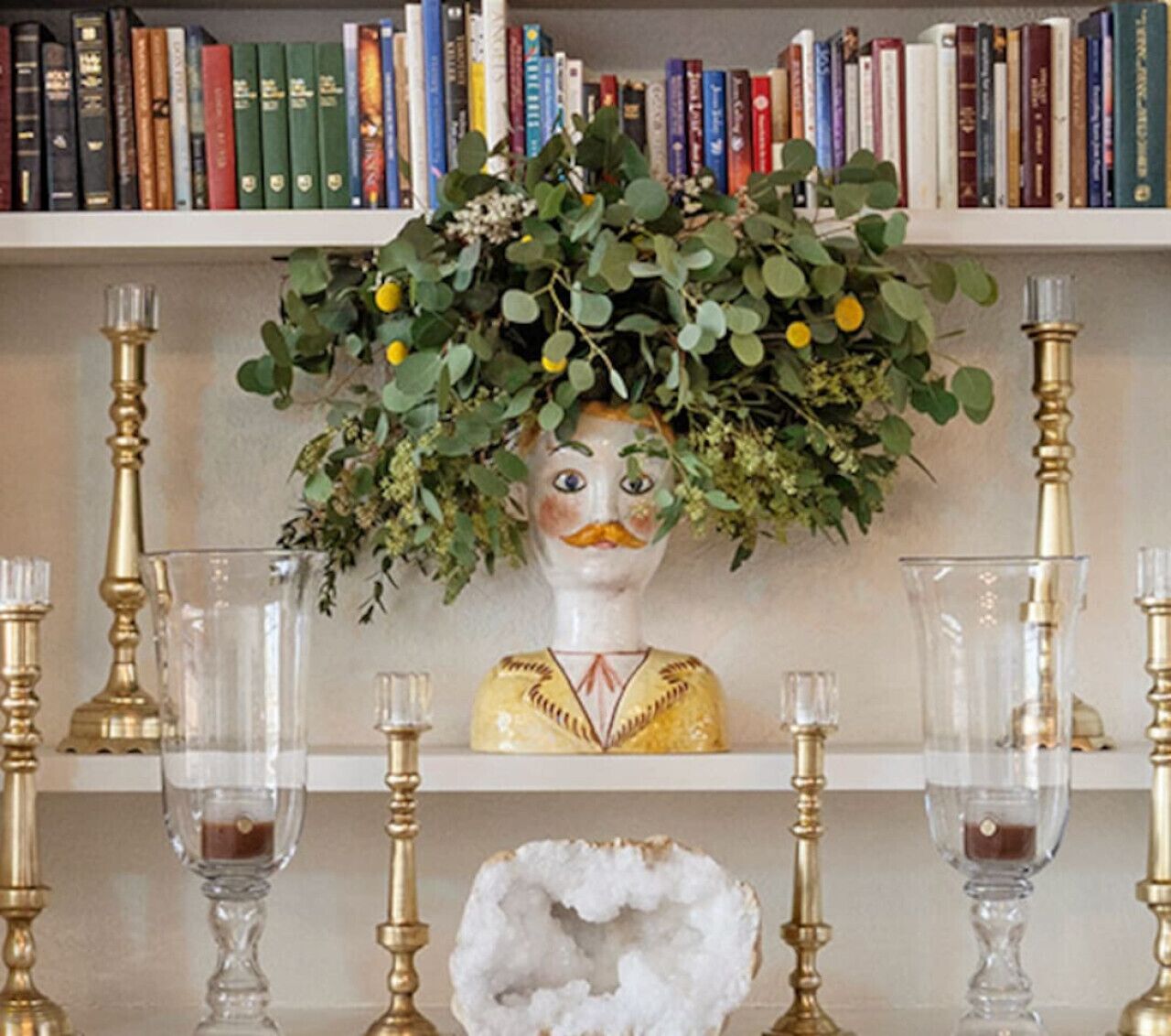 A bookshelf with a decorative bust and clear glassware.