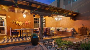 Une terrasse extérieure avec un sol à carreaux, une table entourée de chaises, un canapé et un mur décoratif orné de chapeaux.