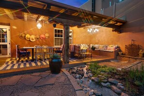 An outdoor patio with a checkered floor, a table with chairs, a sofa, and a decorative wall with hats. - Cinco Chimineas- Indoor Pool, Walk to Plaza (Santa Fe)