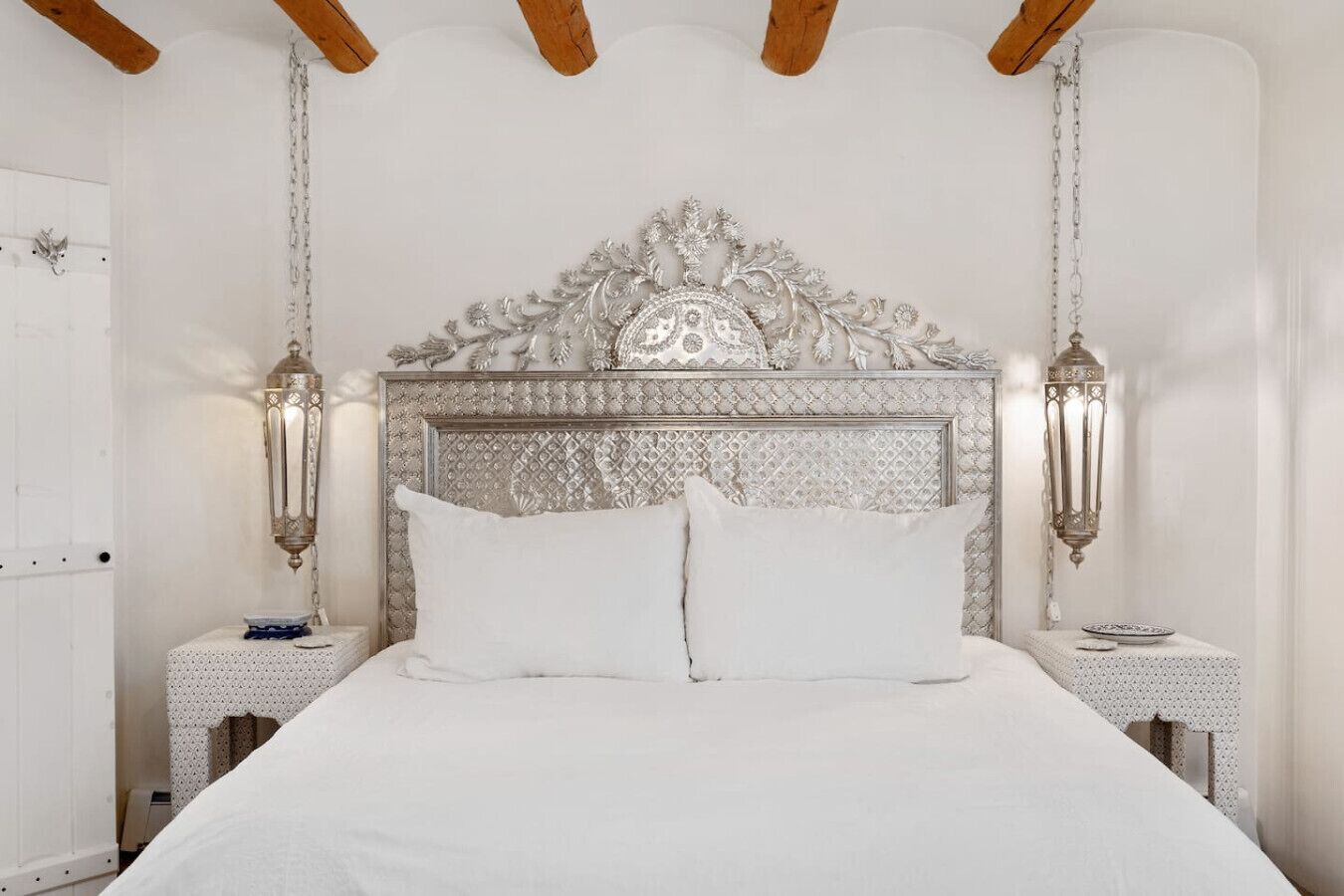 A bedroom with a large bed, ornate headboard, two bedside tables, and wall-mounted lamps.