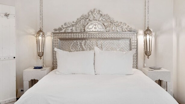 Une chambre à coucher avec un grand lit, une tête de lit décorée, deux tables de chevet et des lampes fixées au mur.