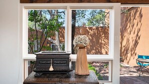 Une fenêtre donnant sur un jardin, avec une statue et un vase décoratif posé sur une table.