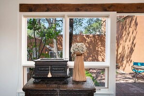 A window with a view of a garden, a statue, and a decorative urn on a table. - Cinco Chimineas- Indoor Pool, Walk to Plaza (Santa Fe)