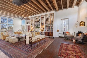 A spacious living room with a fireplace, bookshelves, and a large window. - Cinco Chimineas- Indoor Pool, Walk to Plaza (Santa Fe)