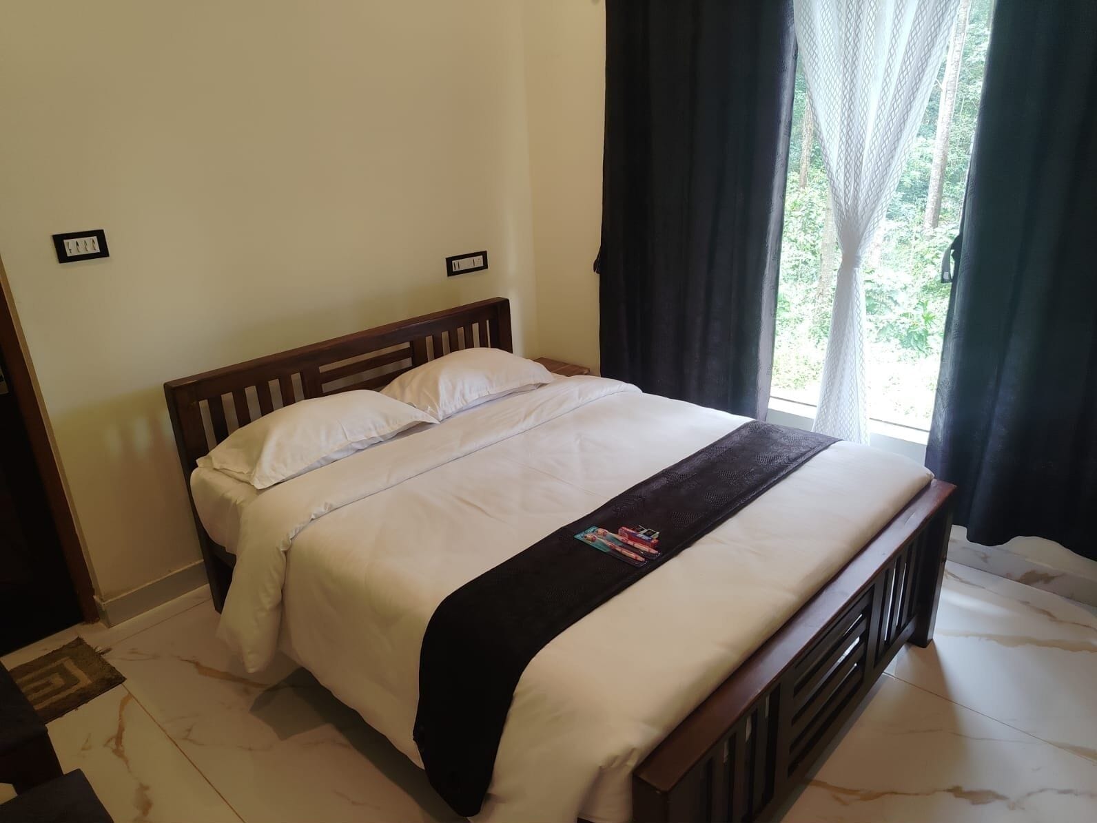 A neatly made bed with a wooden headboard, white bedding, and a black throw blanket.