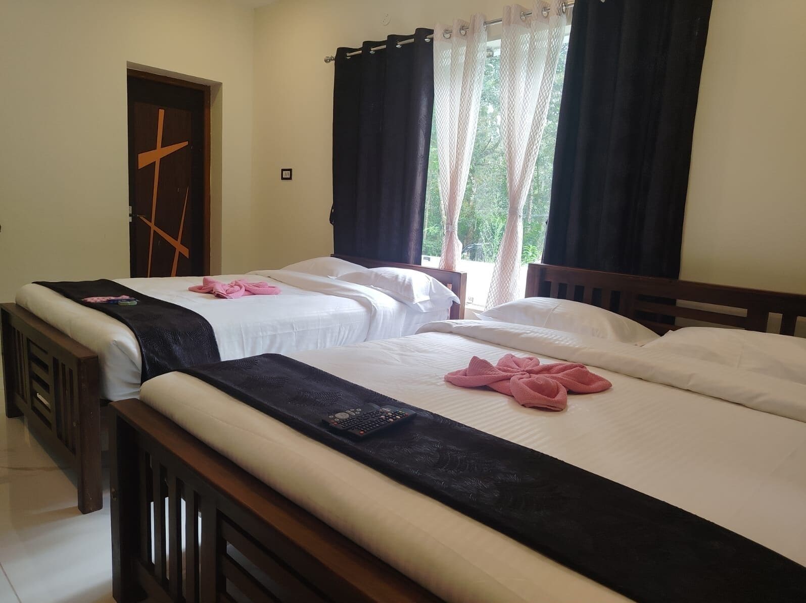 Een hotelkamer met twee bedden, een houten hoofdbord, een kruis op de deur en een raam met gordijnen.