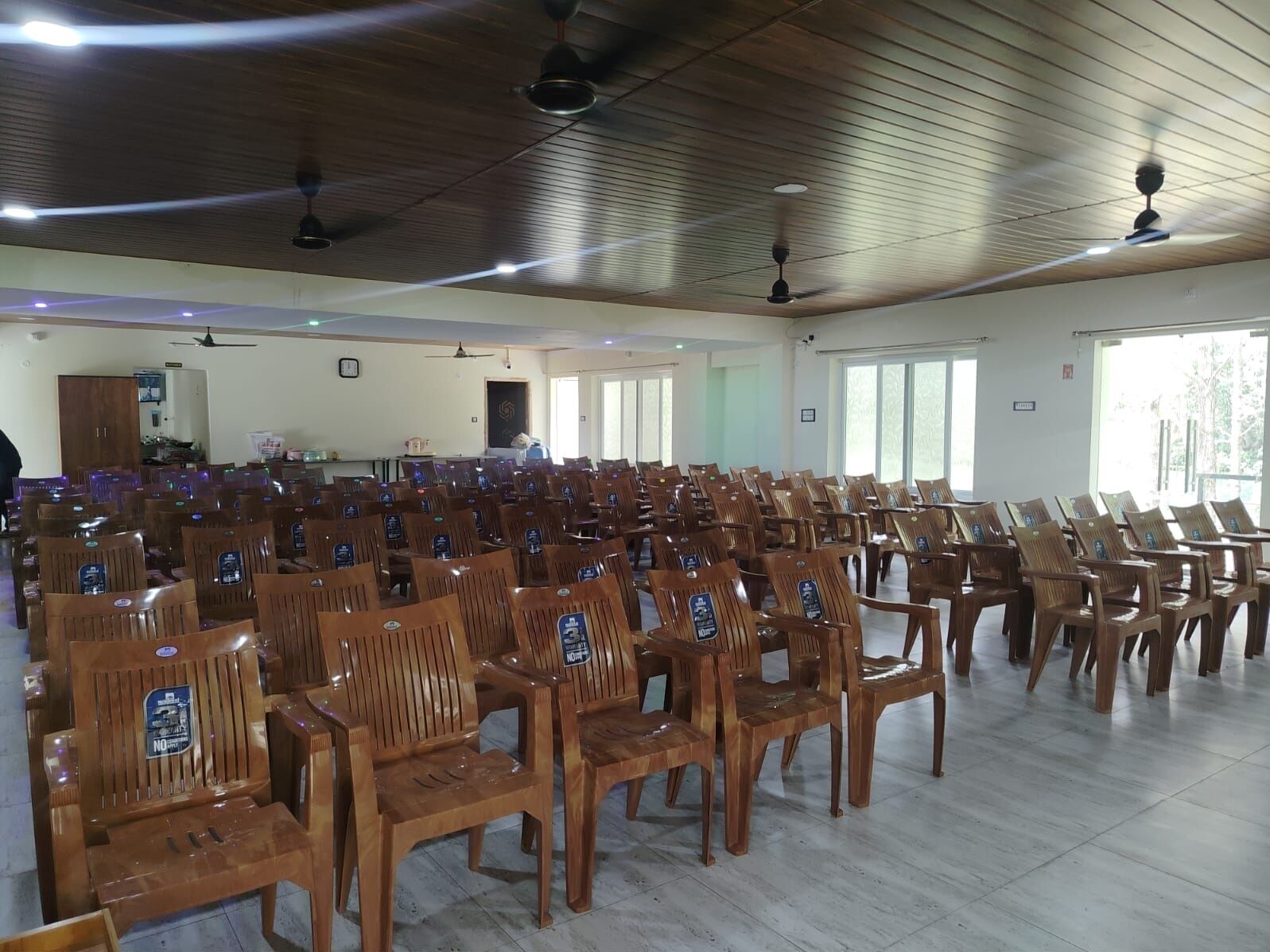 A large hall with rows of wooden chairs and ceiling fans.
