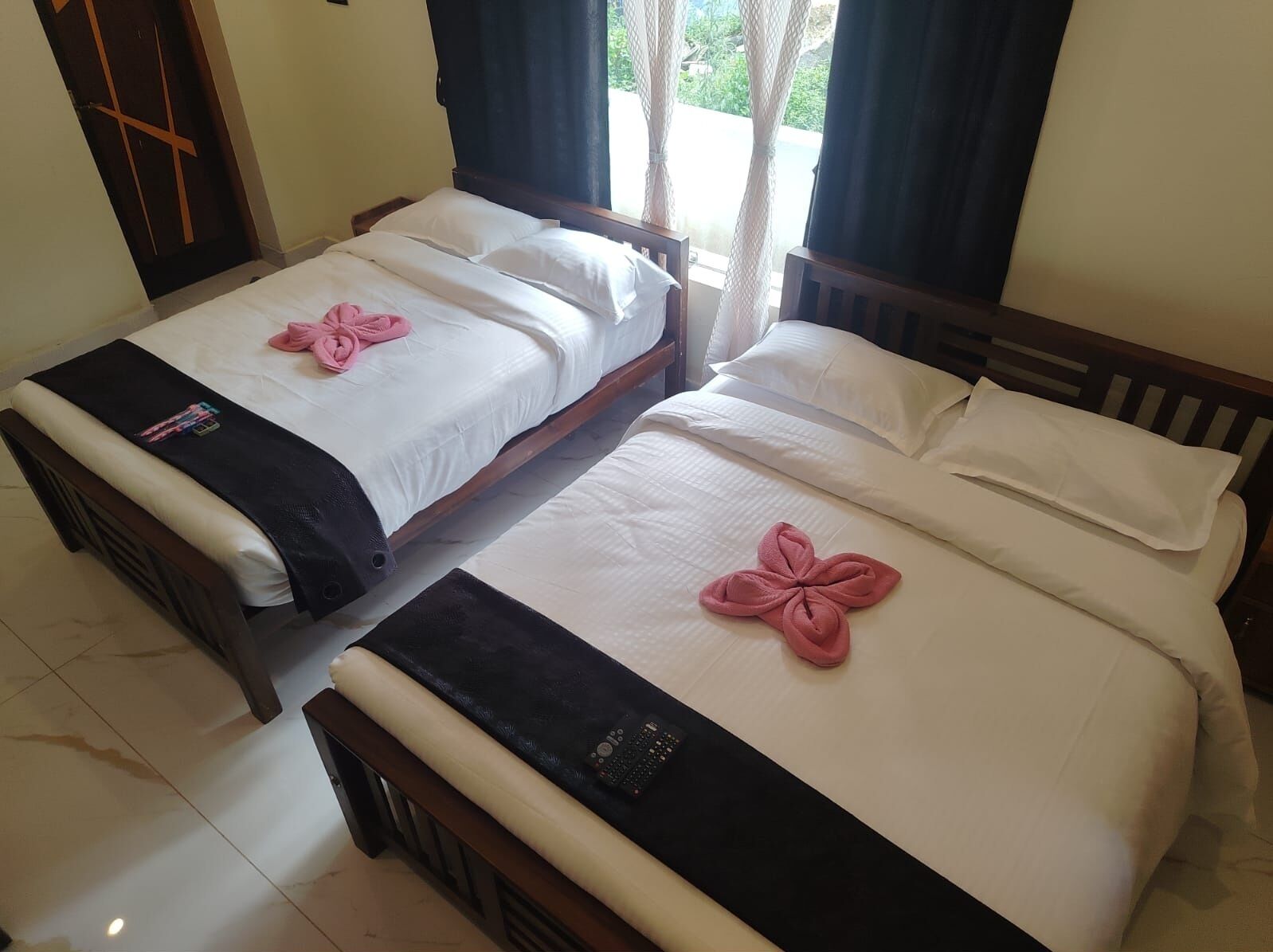 Two single beds with white linens and pink towels, a wooden headboard, and a tiled floor.