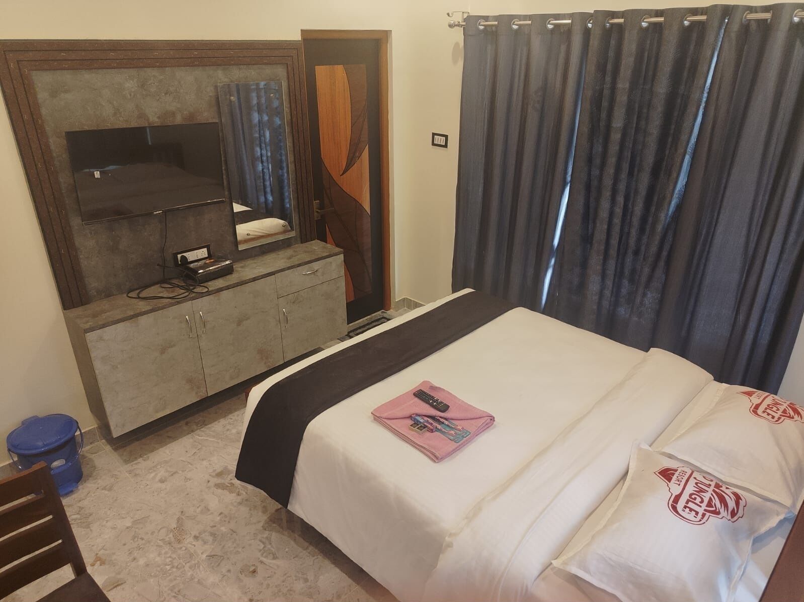 A hotel room with a bed, a dresser, a mirror, and a curtain.