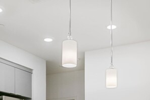 Una cocina moderna con luces colgantes, armarios blancos y un diseño limpio y minimalista.