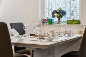 A dining table set with glassware, plates, and cutlery, with a vase of flowers and a window with decorative glass panes in the background. - Bright 3BR/3BA San Jose Townhome | Great Location (San Jose)