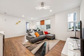 Una sala de estar moderna con un sofá seccional gris, un televisor de pantalla plana y un ventanal con vistas a árboles.