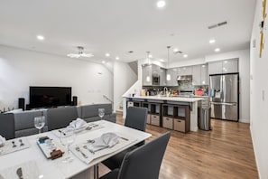 A modern kitchen with stainless steel appliances, a dining area with a white table set for two, and a grey sofa. - Bright 3BR/3BA San Jose Townhome | Great Location (San Jose)