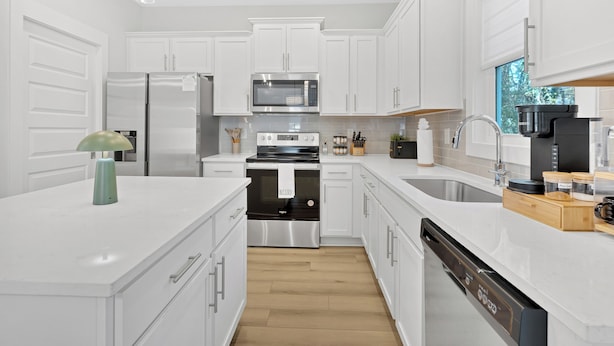 Une cuisine moderne avec des meubles blancs, des appareils électroménagers en acier inoxydable et un plancher en bois.