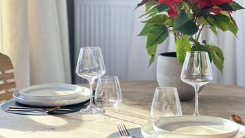 A dining table set with plates, cutlery, and wine glasses, with a potted plant in the background.
