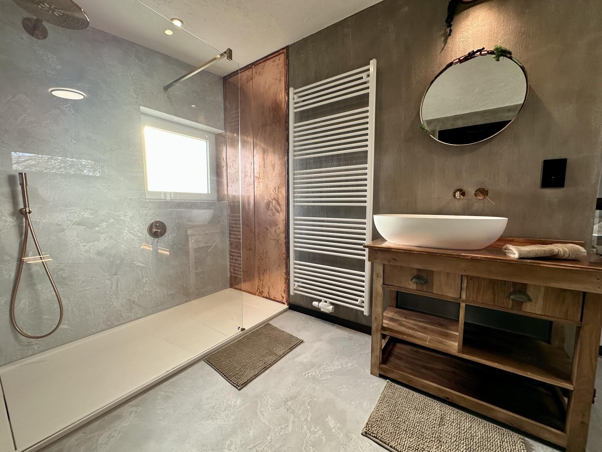 Een moderne badkamer met een inloopdouche, een grote spiegel en een houten wastafelmeubel.